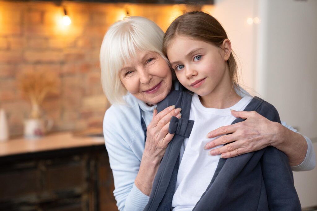 Mature grandmother hugging her granddaughter in kithen with look in camera